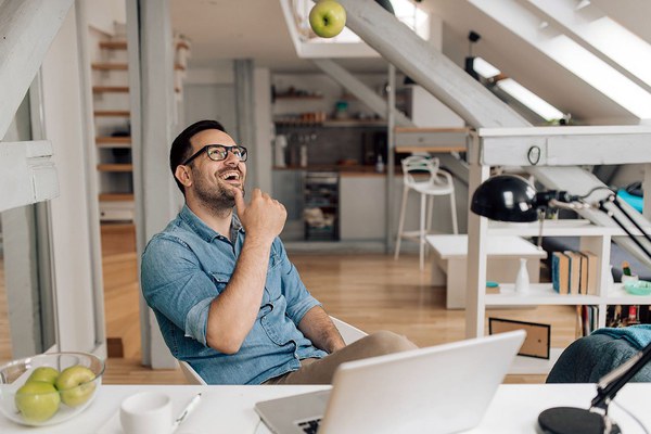 Young man relaxing after work and throwing an apple at his home office.