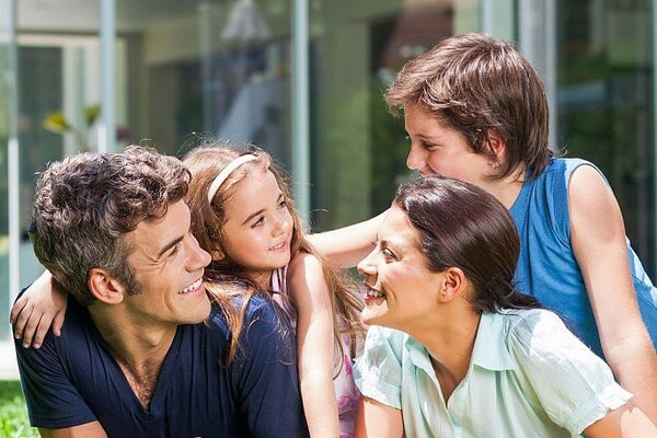 happy family lying  on grass in front of house, parents with two children smile